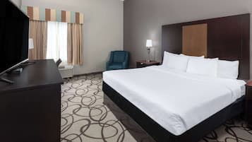 A hotel room with a large bed, a desk with a computer, a chair, and a lamp.