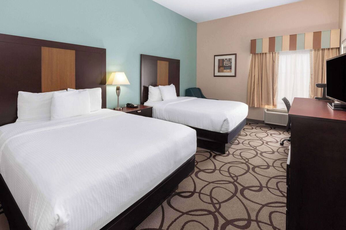 Ein Hotelzimmer mit zwei Betten, einem Schreibtisch, einem Sessel, einem Fernseher und einem Fenster mit Vorhängen.