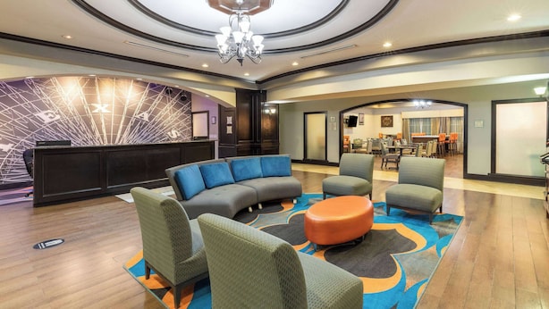 Un hall d’entrée avec un comptoir de réception, un canapé gris aux lignes courbes, des fauteuils verts et un pouf orange.