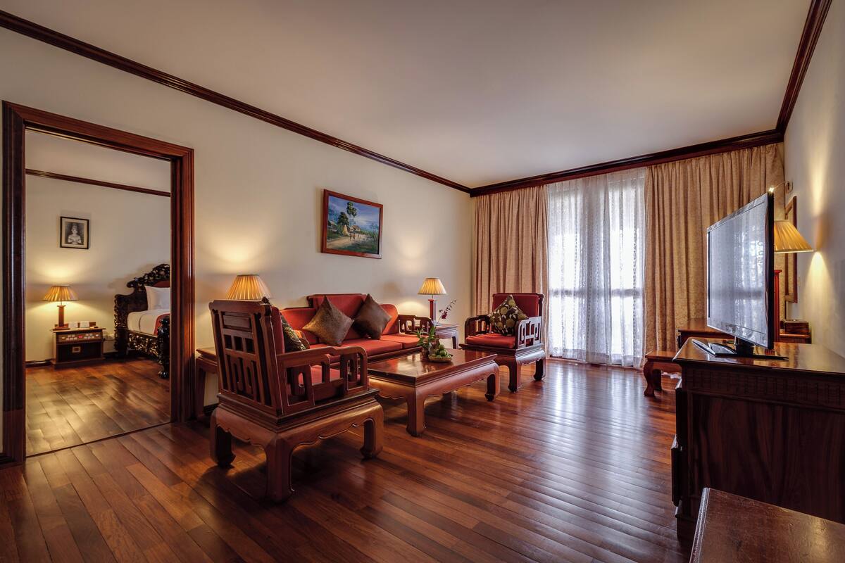 A spacious living room with wooden flooring, a red sofa, a wooden coffee table, and a television.