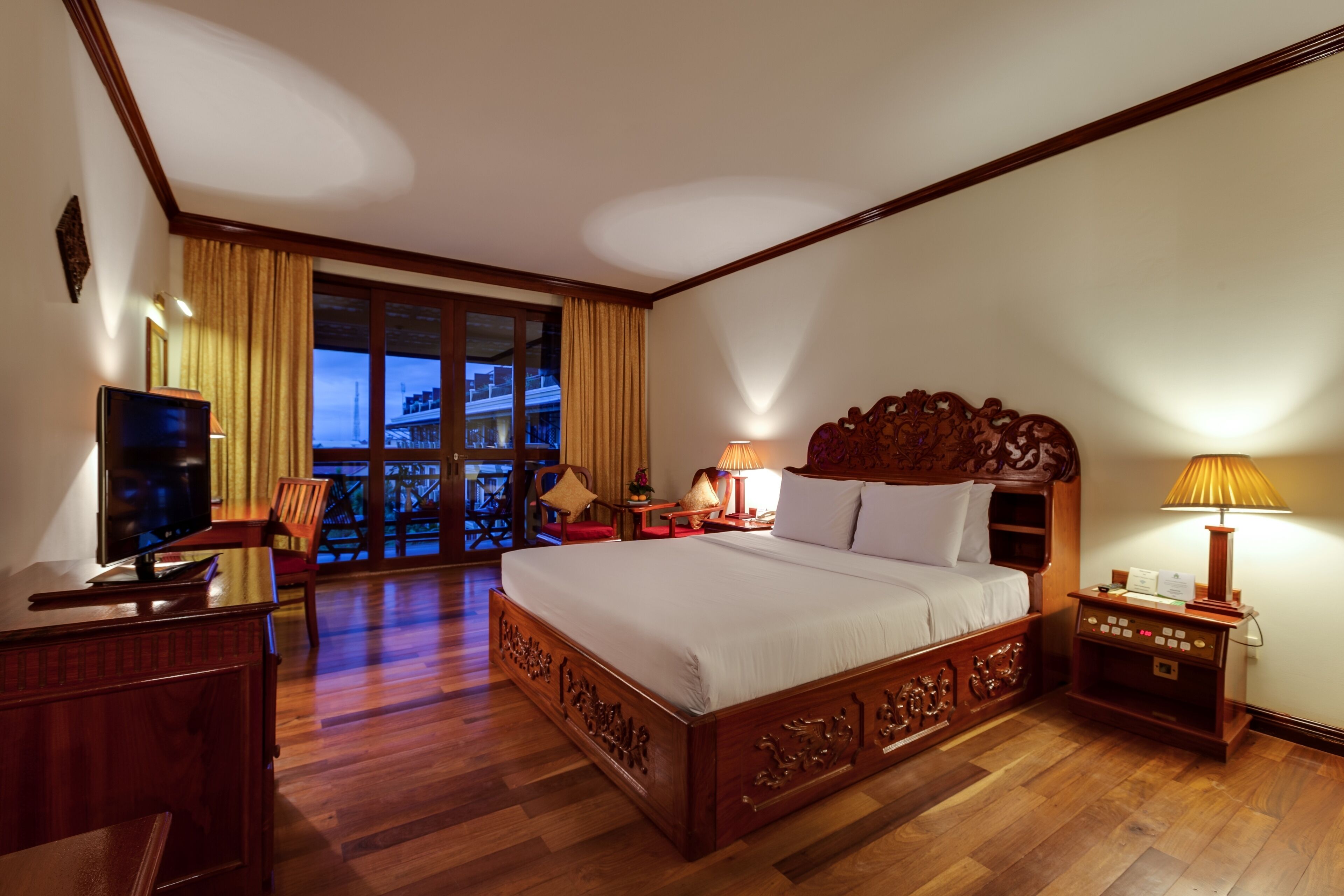 A hotel room with a large bed, wooden furniture, a TV, and a balcony with curtains.