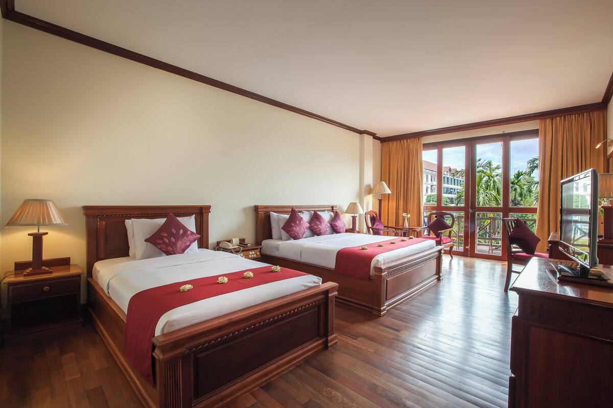 A hotel room with two wooden beds, a desk, a chair, and a television.
