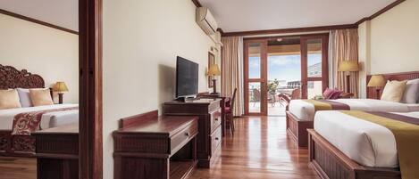 A hotel room with two beds, a TV, wooden furniture, and a view of the city through large windows.
