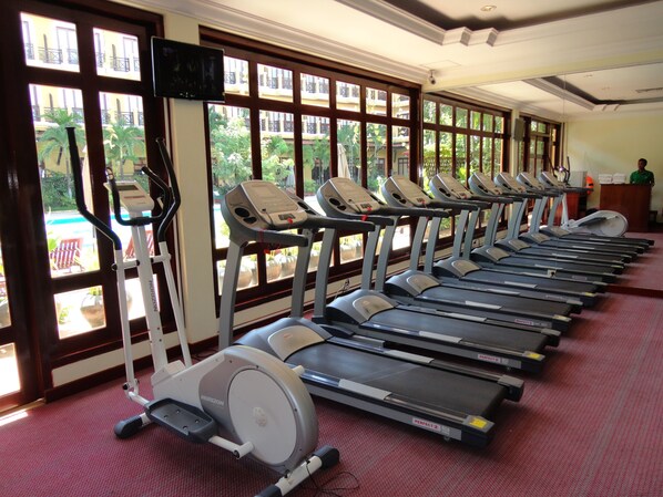 A row of treadmills in a gym with large windows overlooking a courtyard.