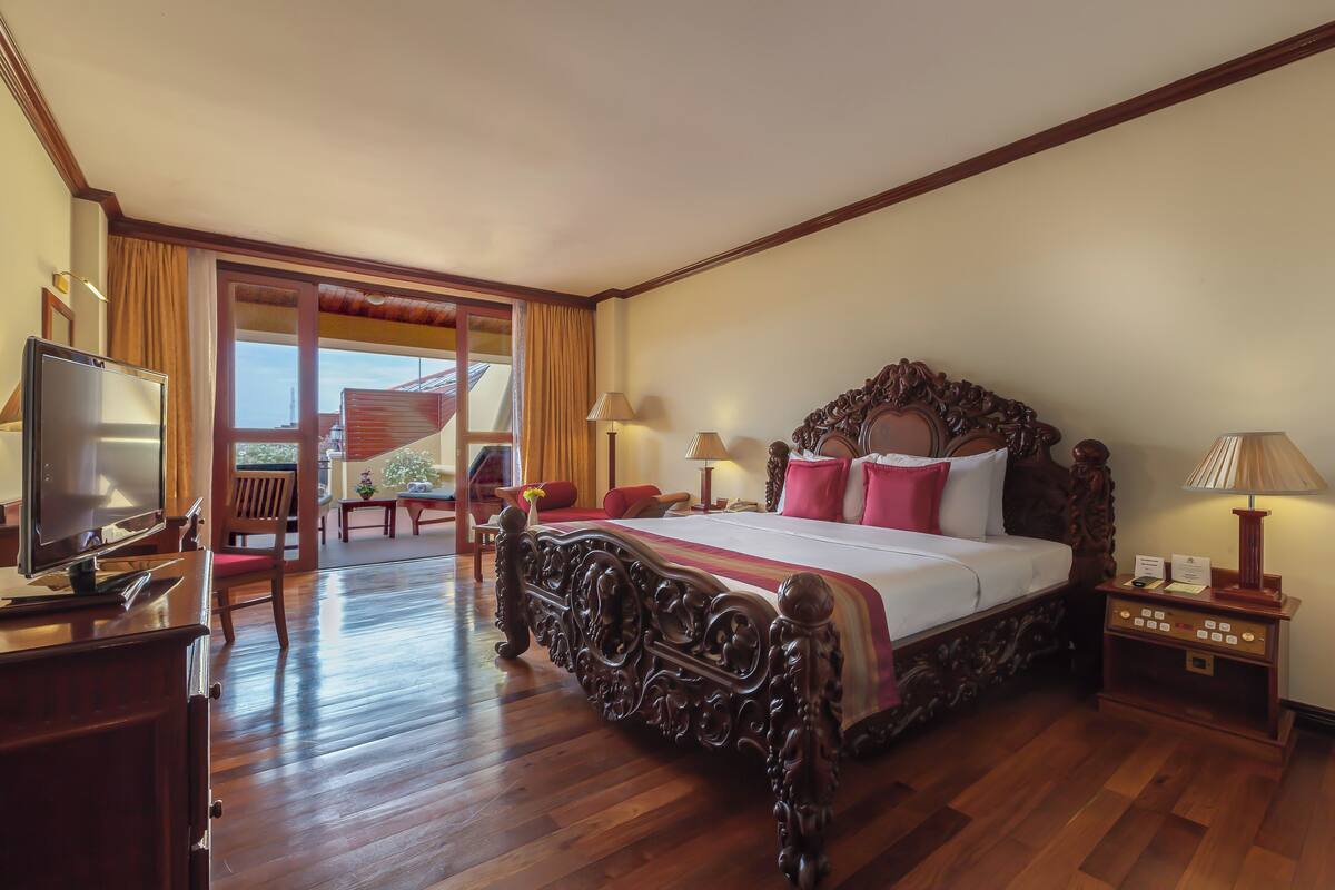 A spacious bedroom with a large bed, wooden floor, and a television on a desk.