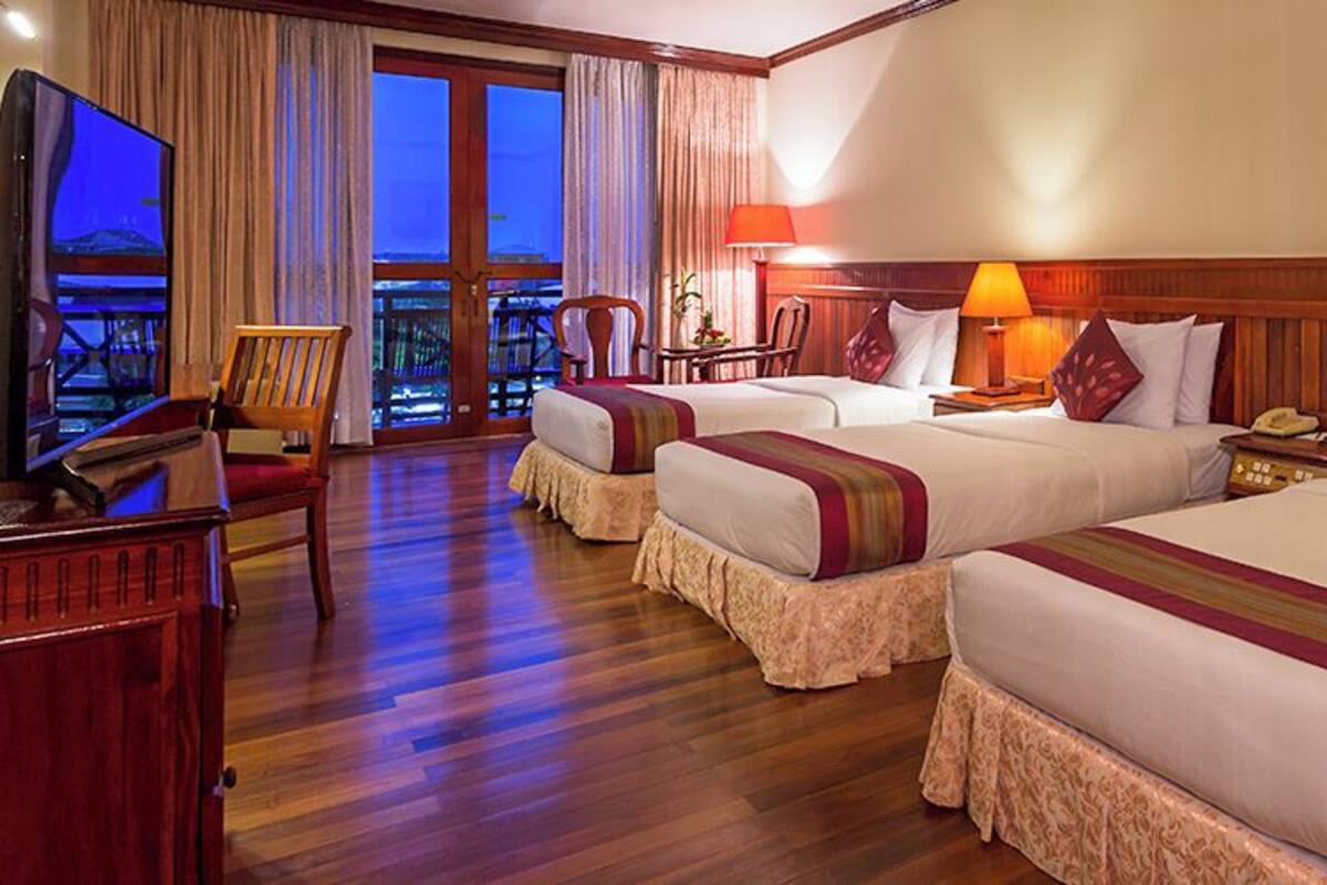 A hotel room with two beds, wooden flooring, a TV, a desk, and a balcony with curtains.