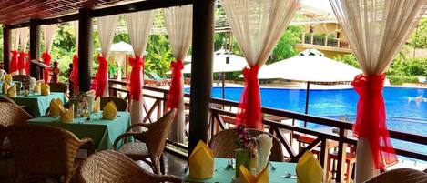 A restaurant with tables set for dining, overlooking a pool.