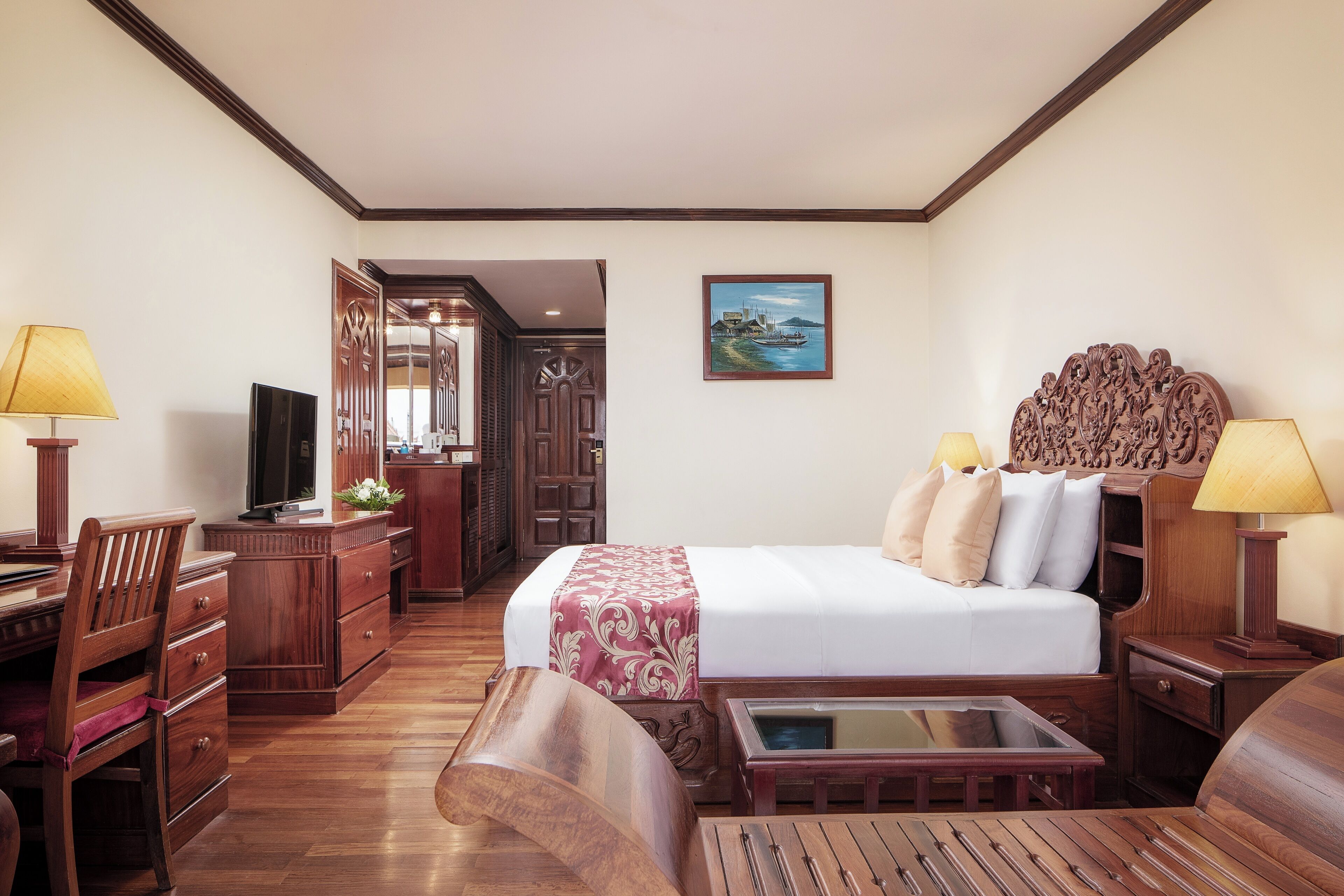 A hotel room with a bed, wooden furniture, a TV, and a painting on the wall.