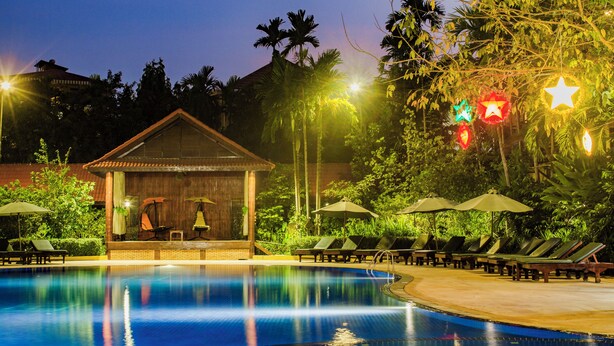 A pool area with lounge chairs and umbrellas, a small wooden structure, and palm trees. - Angkor Paradise Hotel (Siem Reap)