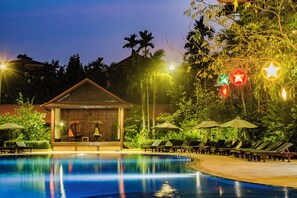 A pool area with lounge chairs and umbrellas, a small wooden structure, and palm trees.