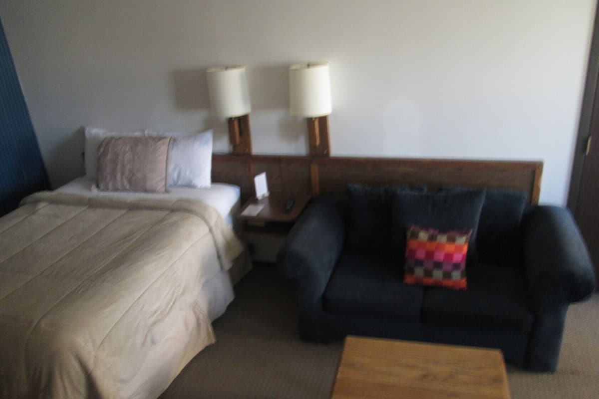 A hotel room with a bed, a nightstand, a lamp, a couch, and a wooden coffee table.
