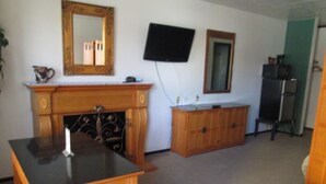 A room with a wooden table, a fireplace, a television mounted on the wall, and a cabinet. - Jim Butler Inn & Suites (Tonopah)