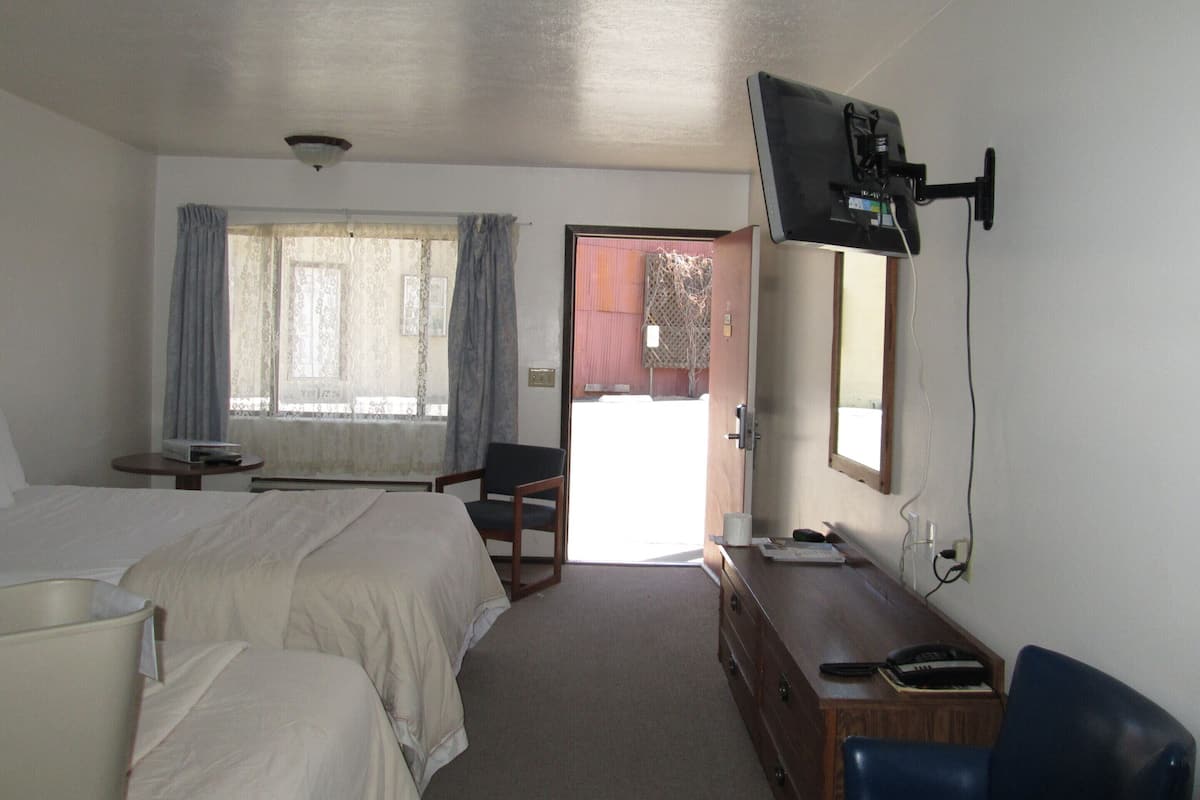 A hotel room with two beds, a desk with a computer, a chair, and a television mounted on the wall.