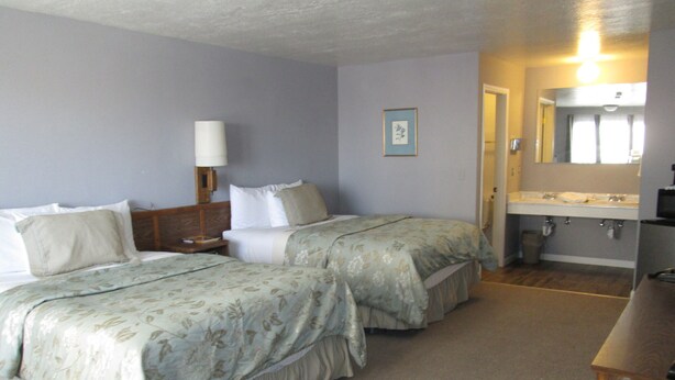 A hotel room with two beds, a nightstand, a lamp, a bathroom with a sink and mirror, and a wooden desk. - Jim Butler Inn & Suites (Tonopah)