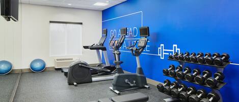 Un gimnasio con equipo de ejercicio, una pared con mensajes motivacionales y un estante con mancuernas.