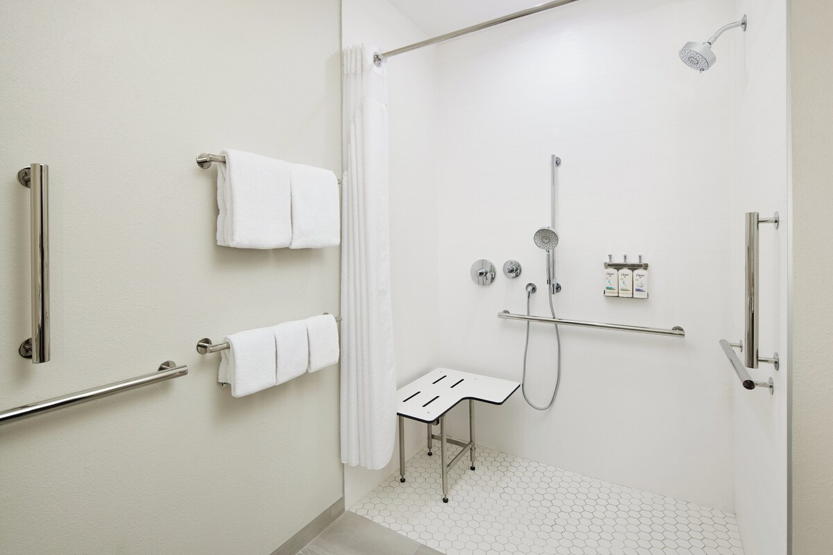 Une salle de bain moderne équipée d’une douche, de barres d’appui, d’une petite table et d’un porte-serviettes.