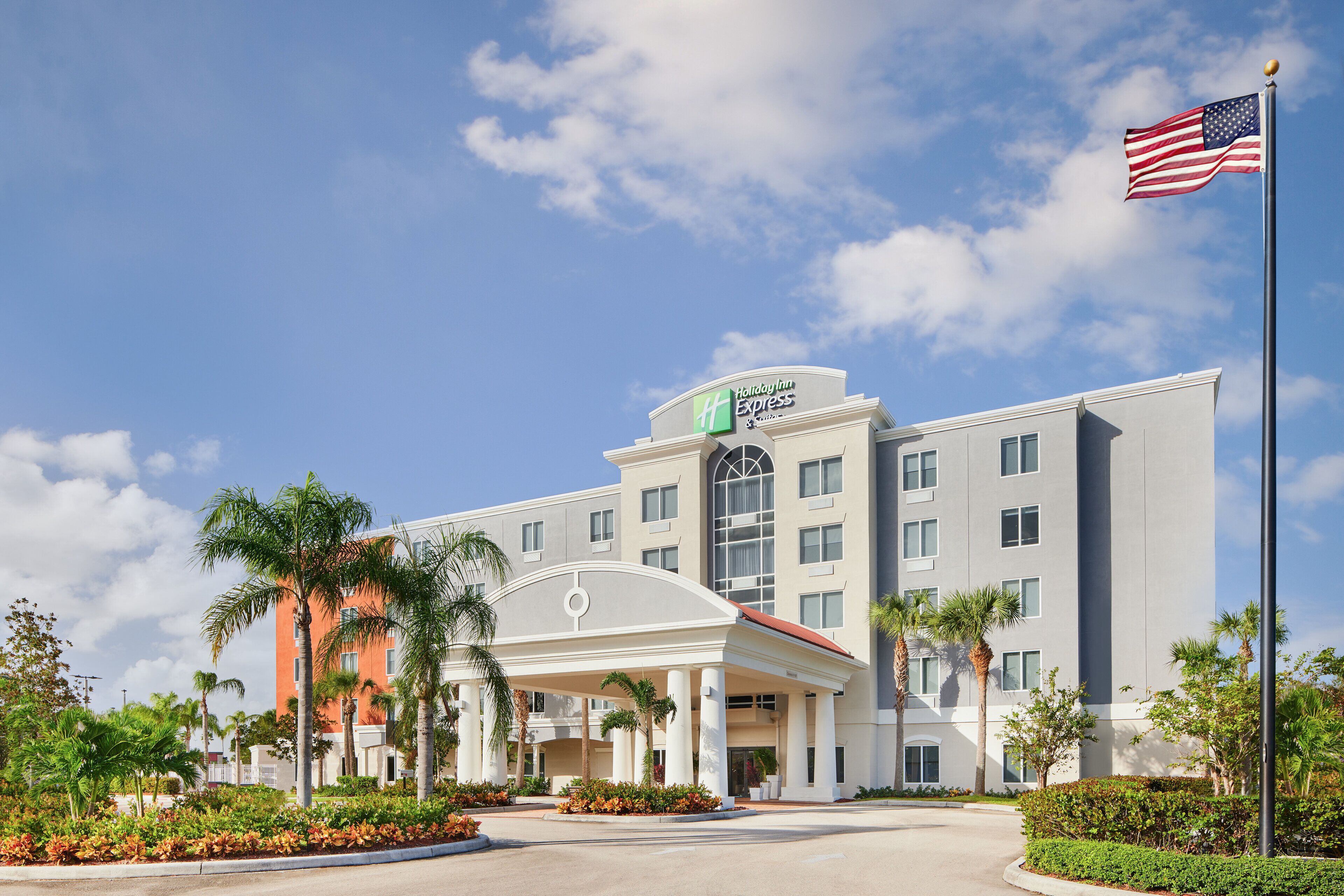 A Holiday Inn Express hotel with a covered entrance, palm trees, and an American flag.