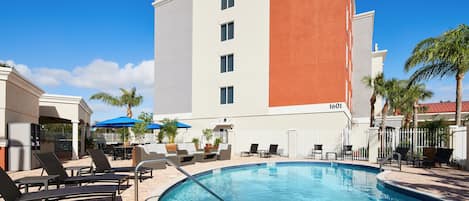 A hotel pool area with lounge chairs, umbrellas, and a clear blue sky.