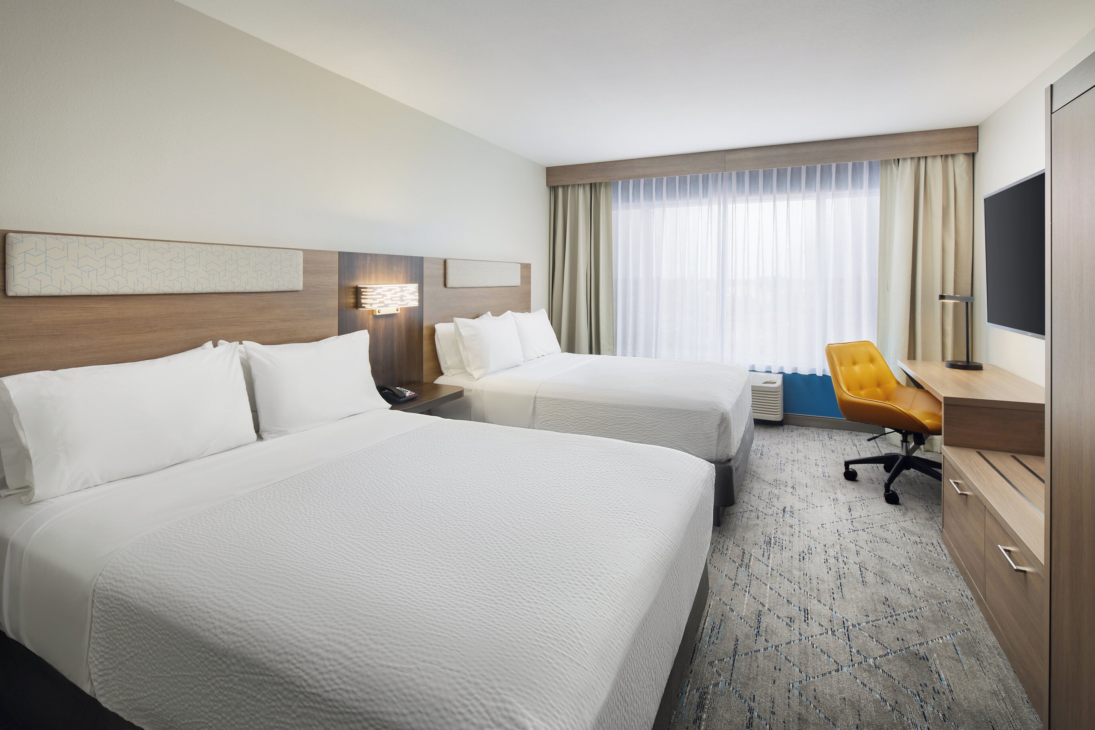 A hotel room with two beds, a desk, a chair, a TV, and a window with curtains.
