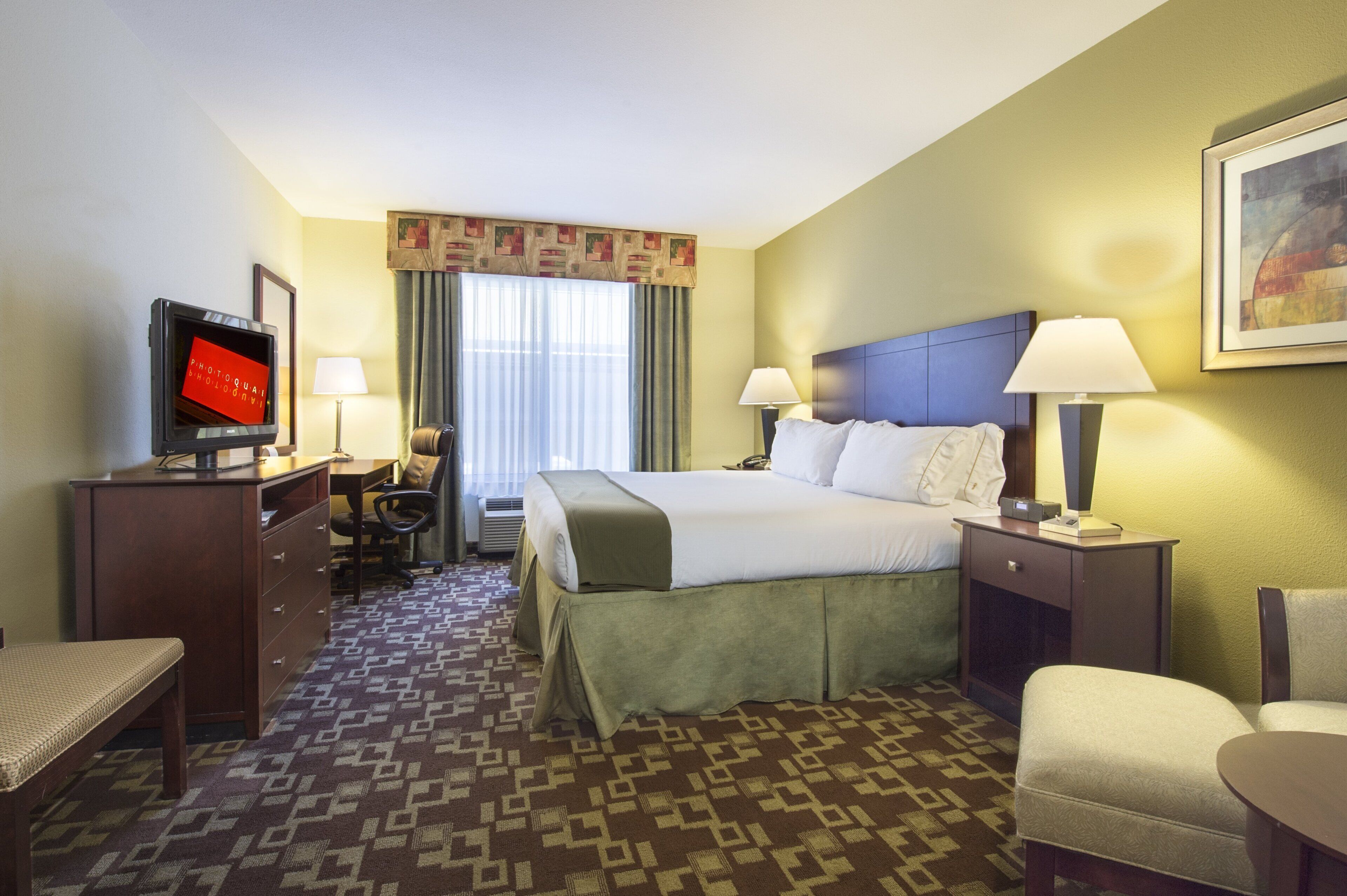 Een hotelkamer met een bed, twee bedlampen, een bureau met een computer, een stoel en een televisie.