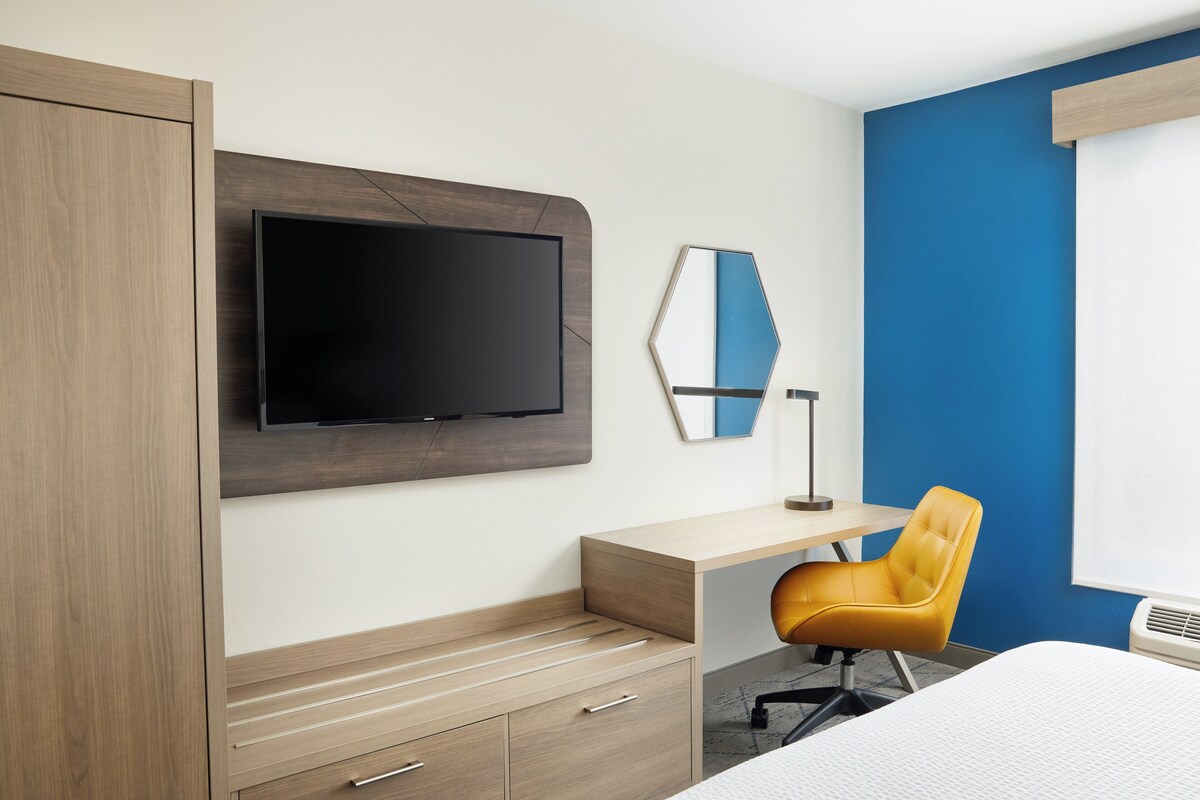 Une chambre d’hôtel comprenant un lit, un bureau, une chaise, une télévision et une armoire.