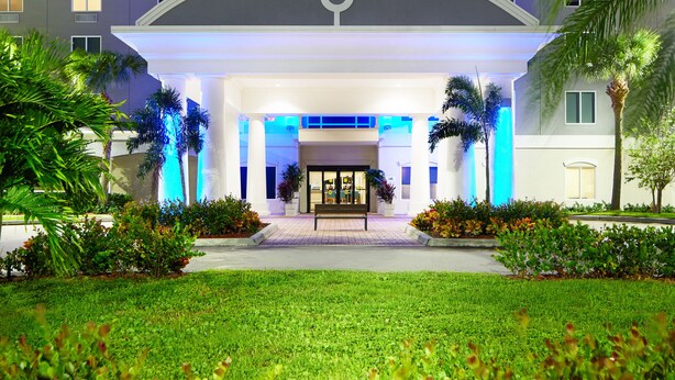 Un hotel Holiday Inn Express & Suites con diseño moderno, que destaca por su entrada llamativa, jardines bien cuidados y una vista despejada del cielo.