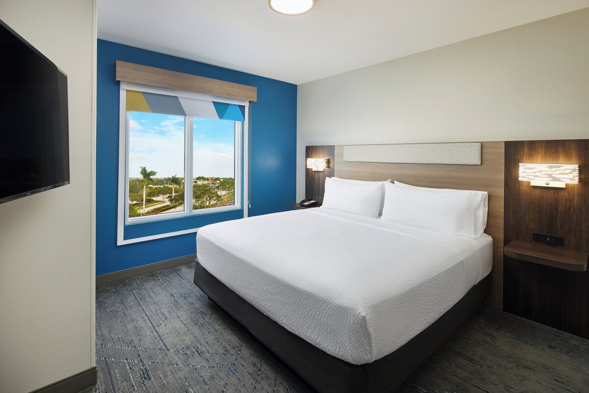 Une chambre d’hôtel moderne, dotée d’un grand lit, d’un téléviseur fixé au mur et d’une fenêtre donnant sur l’extérieur.