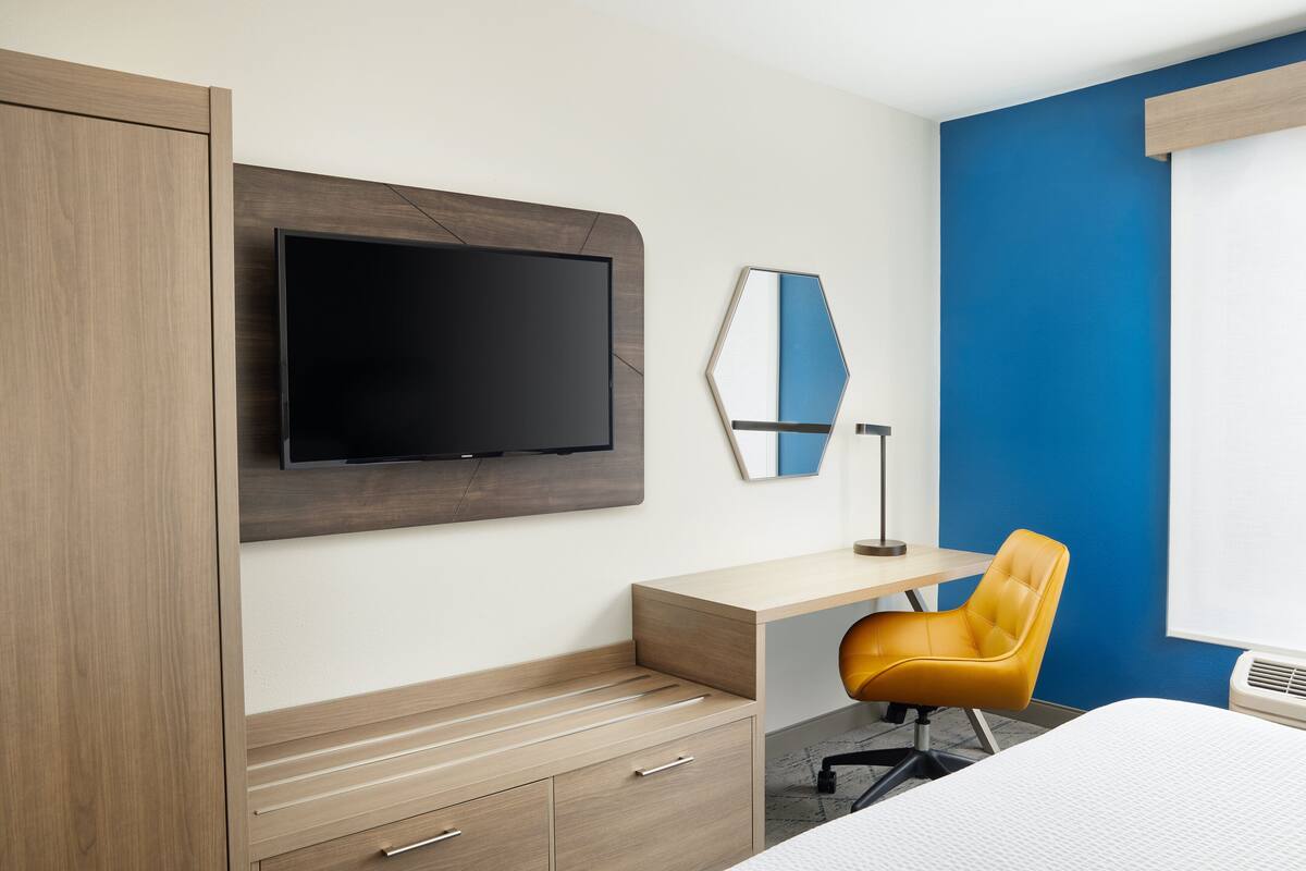 Een hotelkamer met een bed, een bureau, een stoel, een televisie en een kledingkast.