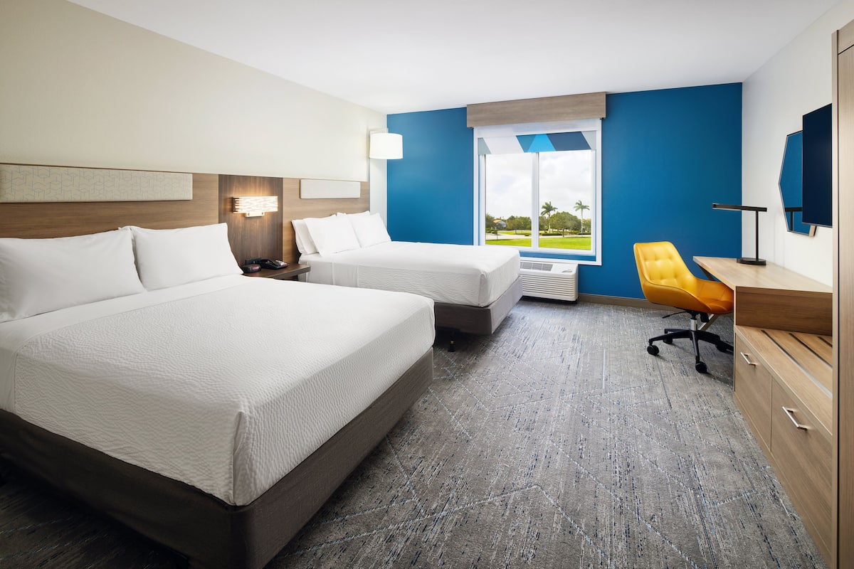 Een hotelkamer met twee bedden, een bureau, een stoel en een groot raam met uitzicht.