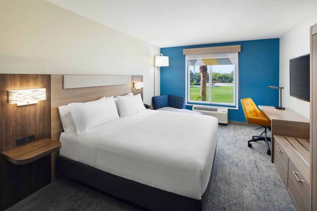Hotelkamer met een groot bed, een bureau, een stoel, een televisie en een raam met uitzicht op groen.