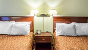 A hotel room with two beds, each with a patterned bedspread and white pillows. There is a nightstand between the beds with a lamp, a phone, and a small table.