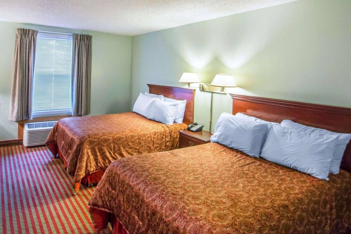 Habitación de hotel con dos camas, una ventana con cortinas, un equipo de aire acondicionado y dos lámparas de noche.