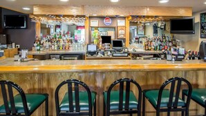 A bar area with a Coors Light sign, multiple liquor bottles, a cash register, and green bar stools. - Rodeway Inn Lakeville - Finger Lakes Area (Lakeville)