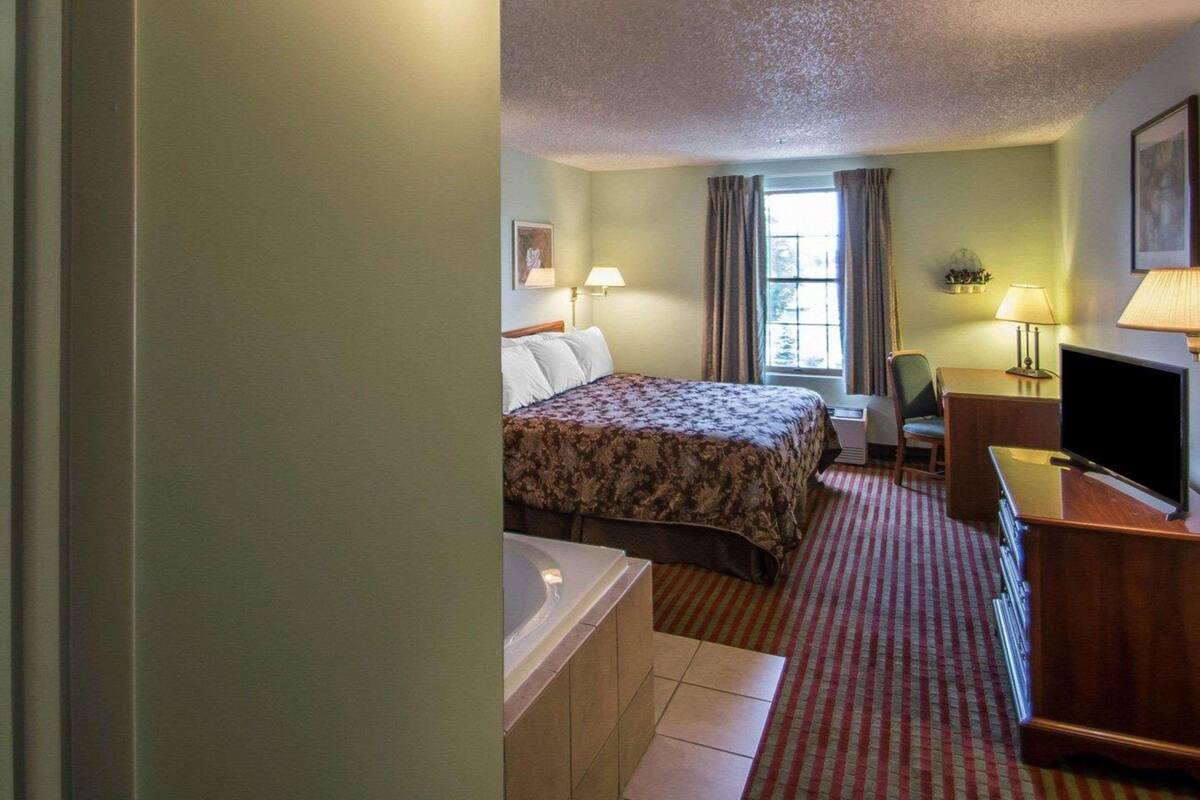 Habitación de hotel con cama, escritorio con computadora, silla, ventana con cortinas y baño con bañera.