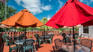 An outdoor patio with tables and chairs, red and orange umbrellas, and a wooden deck. - Rodeway Inn Lakeville - Finger Lakes Area (Lakeville)