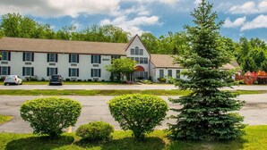 A two-story motel with a red roof and white siding, numbered 6001, featuring a central entrance with a red awning. - Rodeway Inn Lakeville - Finger Lakes Area (Lakeville)