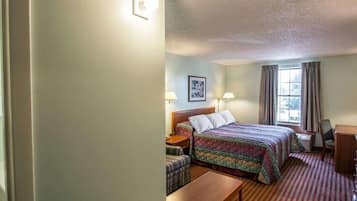 Ein Hotelzimmer mit einem Bett, einem Schreibtisch, einem Stuhl, einem kleinen Tisch und einem Fenster mit Vorhängen.