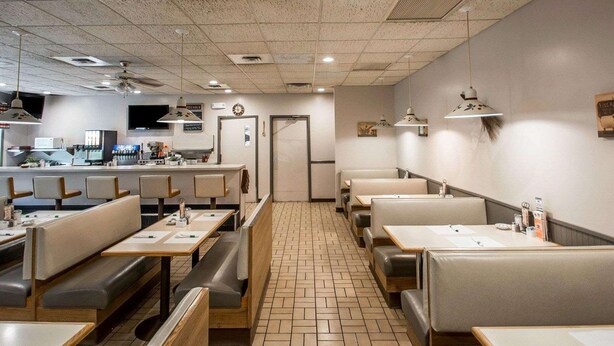 A restaurant with booths and tables, a kitchen area, and a tiled floor. - Rodeway Inn Lakeville - Finger Lakes Area (Lakeville)