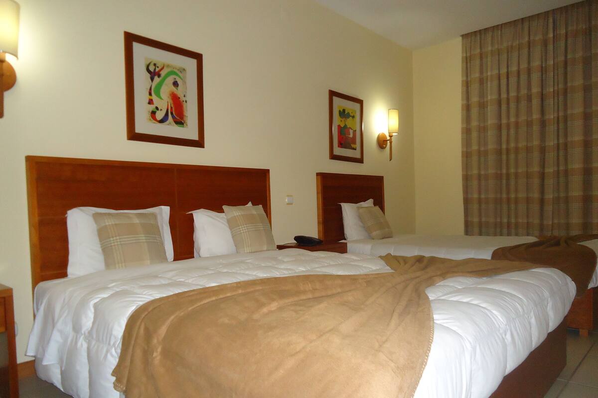 A hotel room with two beds, a wooden headboard, a blue rug, and artwork on the walls.