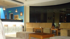 Een moderne hotel lobby met een blauwe accentmuur, een zithoek met banken en fauteuils, een houten salontafel en een receptiebalie.