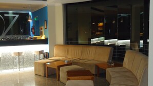 Een moderne lounge met een bank, voetenbankje en salontafel, een bar met krukken, en een groot raam met uitzicht op de stad.