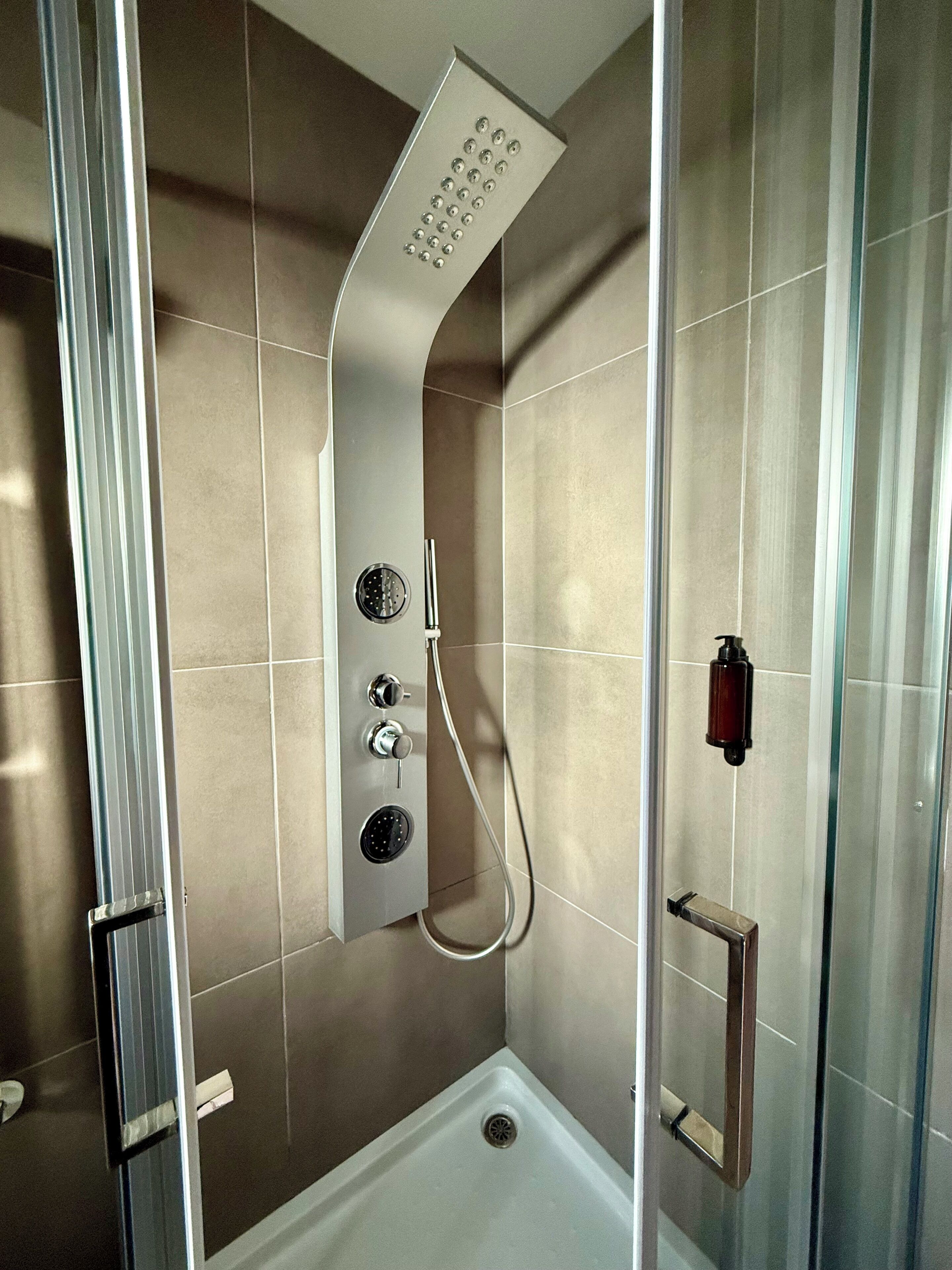 Un box de ducha moderno con cabezal curvo, panel de control y puertas de vidrio.