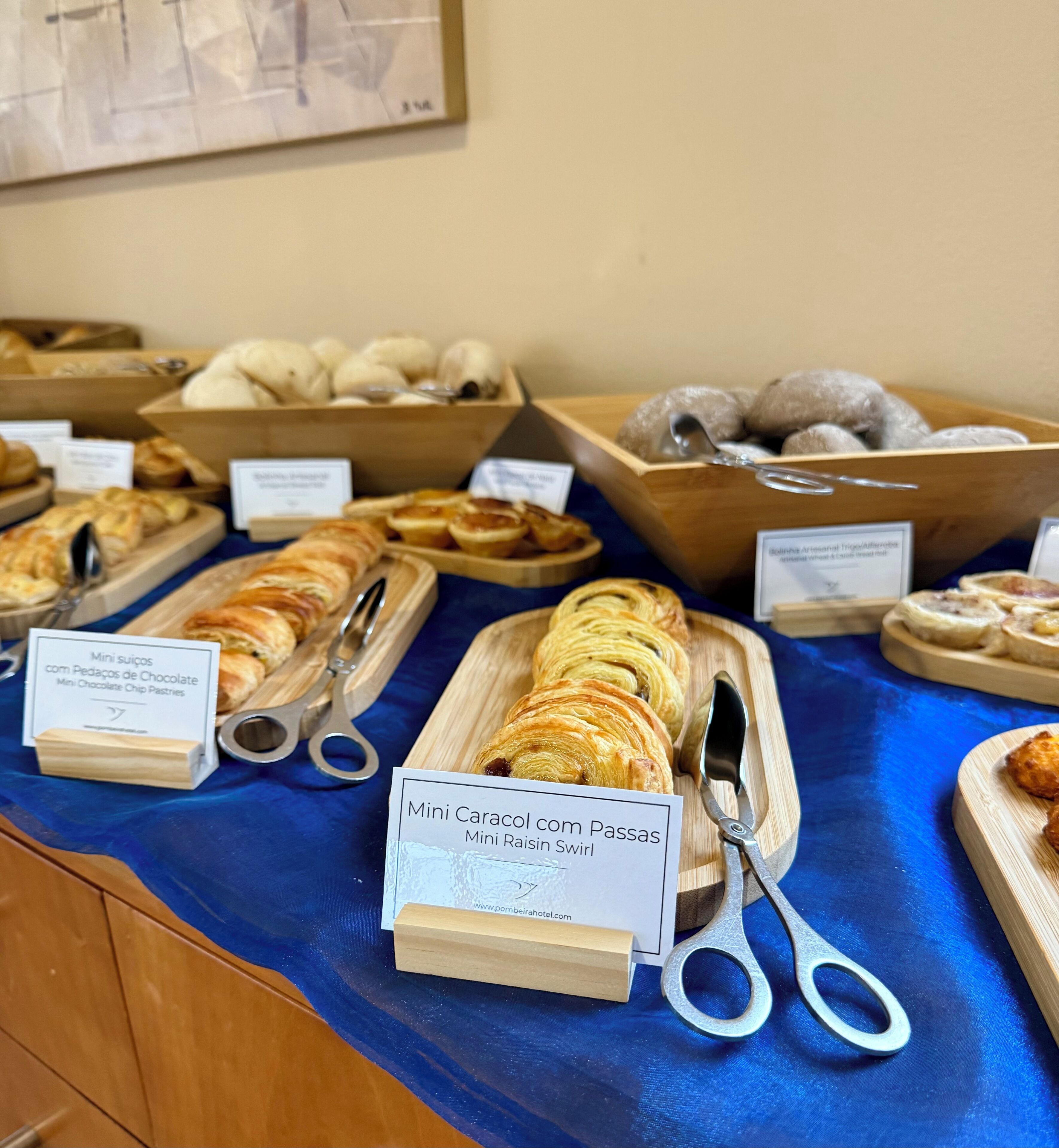 Buffet com diversos pães e doces, incluindo Mini Caracol com Passas e Mini Bolinhos de Chocolate.
