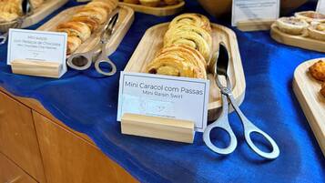 Buffet com diversos pães e doces, incluindo Mini Caracol com Passas e Mini Bolinhos de Chocolate.