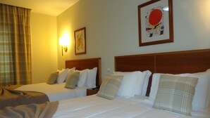 Een hotelkamer met twee bedden, een groot raam met gordijnen, een wandlamp en een ingelijst schilderij.