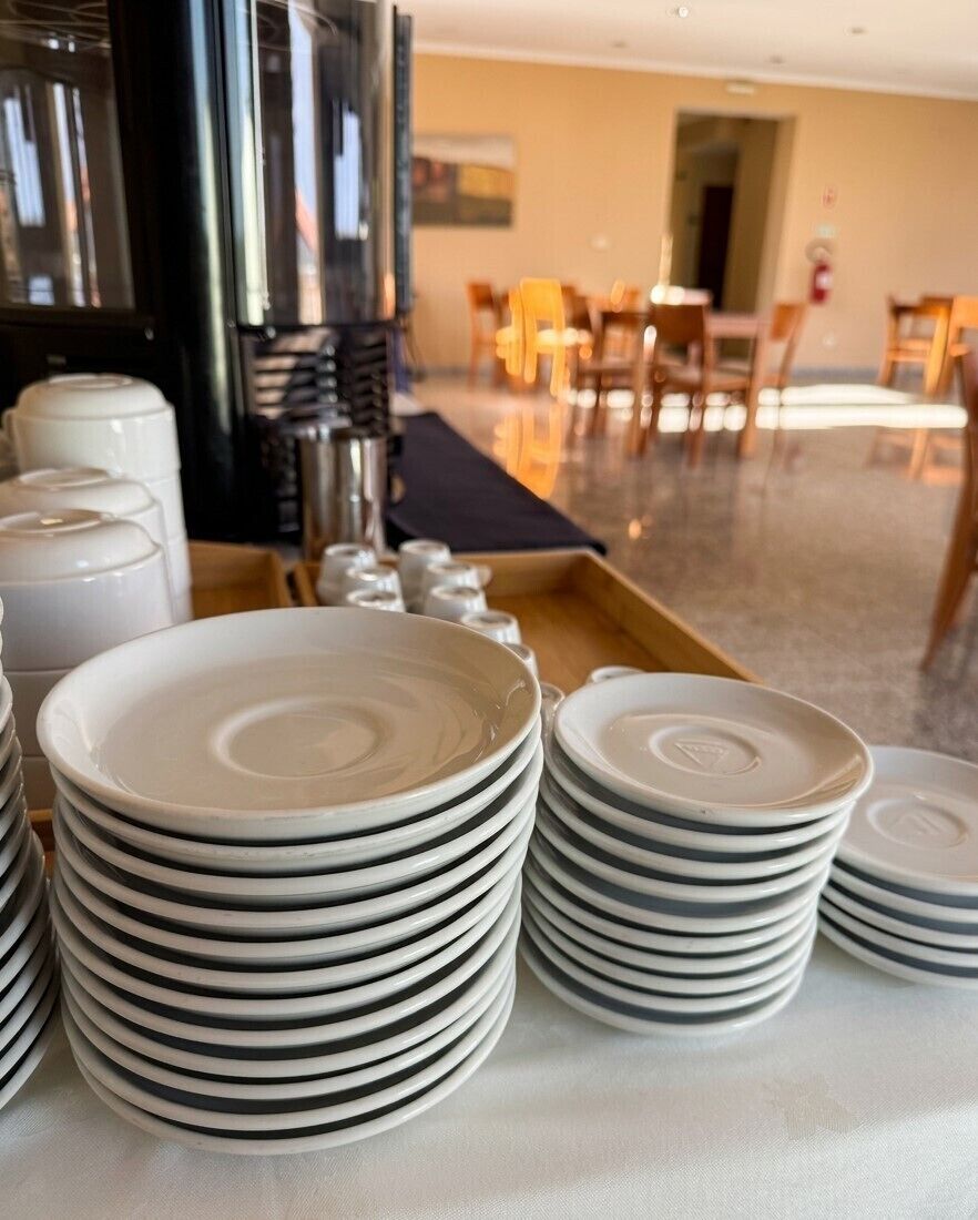 Des piles d’assiettes blanches à rayures noires sont posées sur une table dans la salle à manger d’un hôtel.
