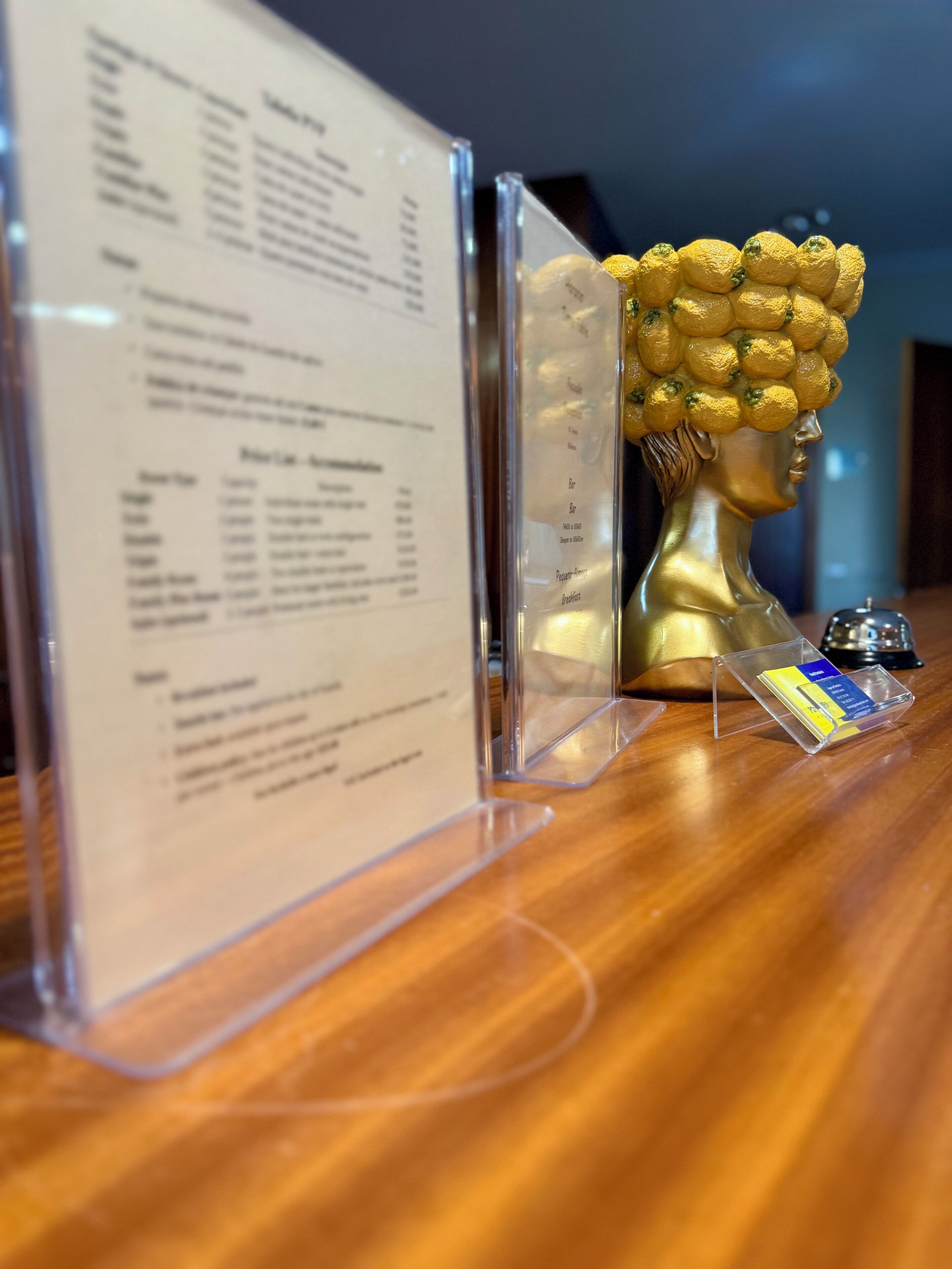 Un mostrador de recepción con un menú, un busto dorado y una pequeña campana.