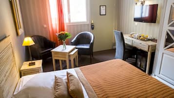 Ein Hotelzimmer mit Bett, Schreibtisch, Stuhl, Fernseher und einem Fenster mit Vorhängen.