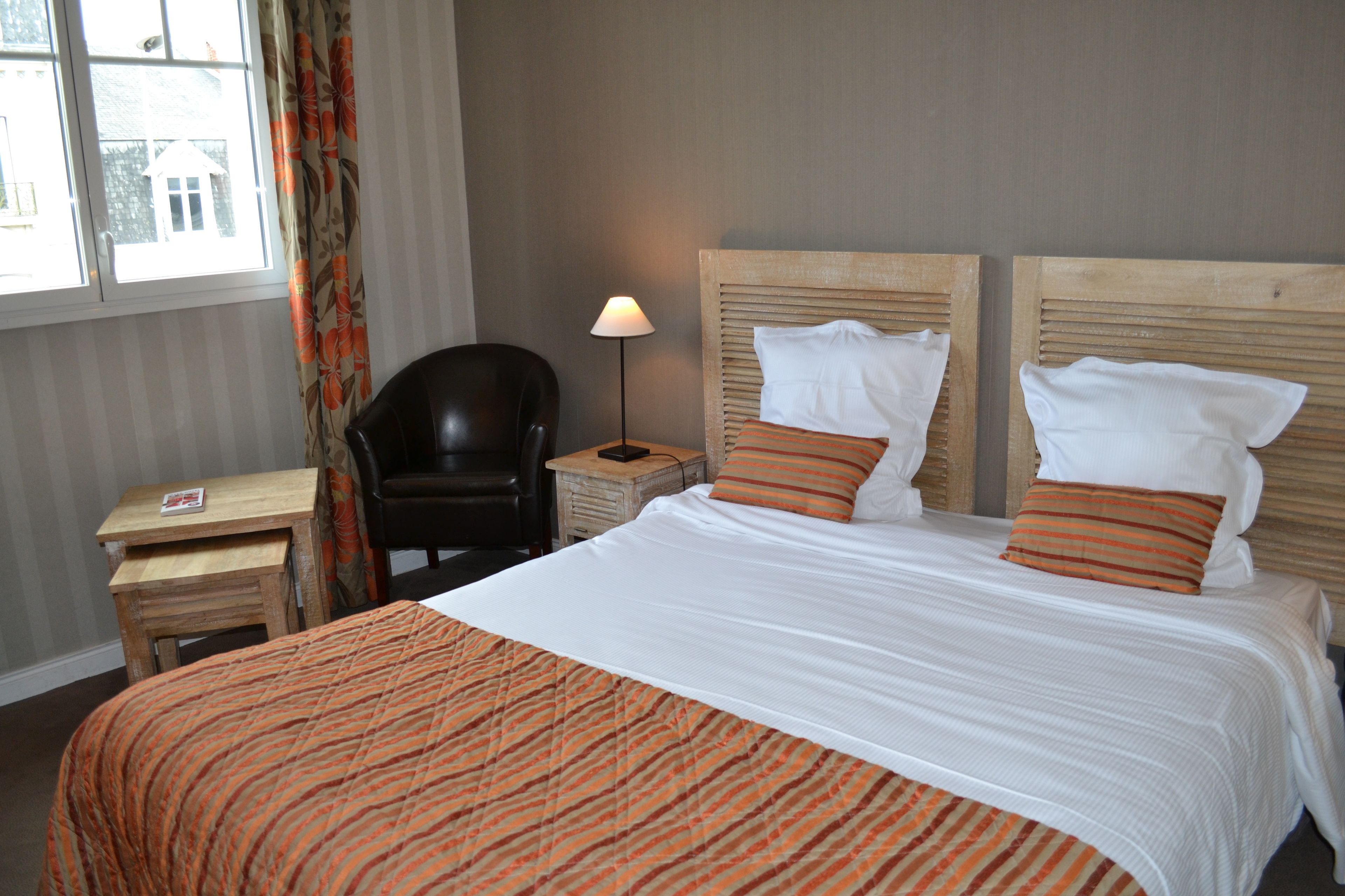 Ein Hotelzimmer mit einem großen Bett, zwei Kissen, einem Sessel, einem Nachttisch und einer Lampe.