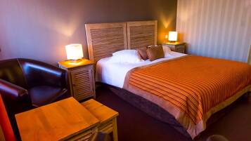 A hotel room with a bed, a wooden headboard, two bedside tables with lamps, a wooden desk, and a leather chair.